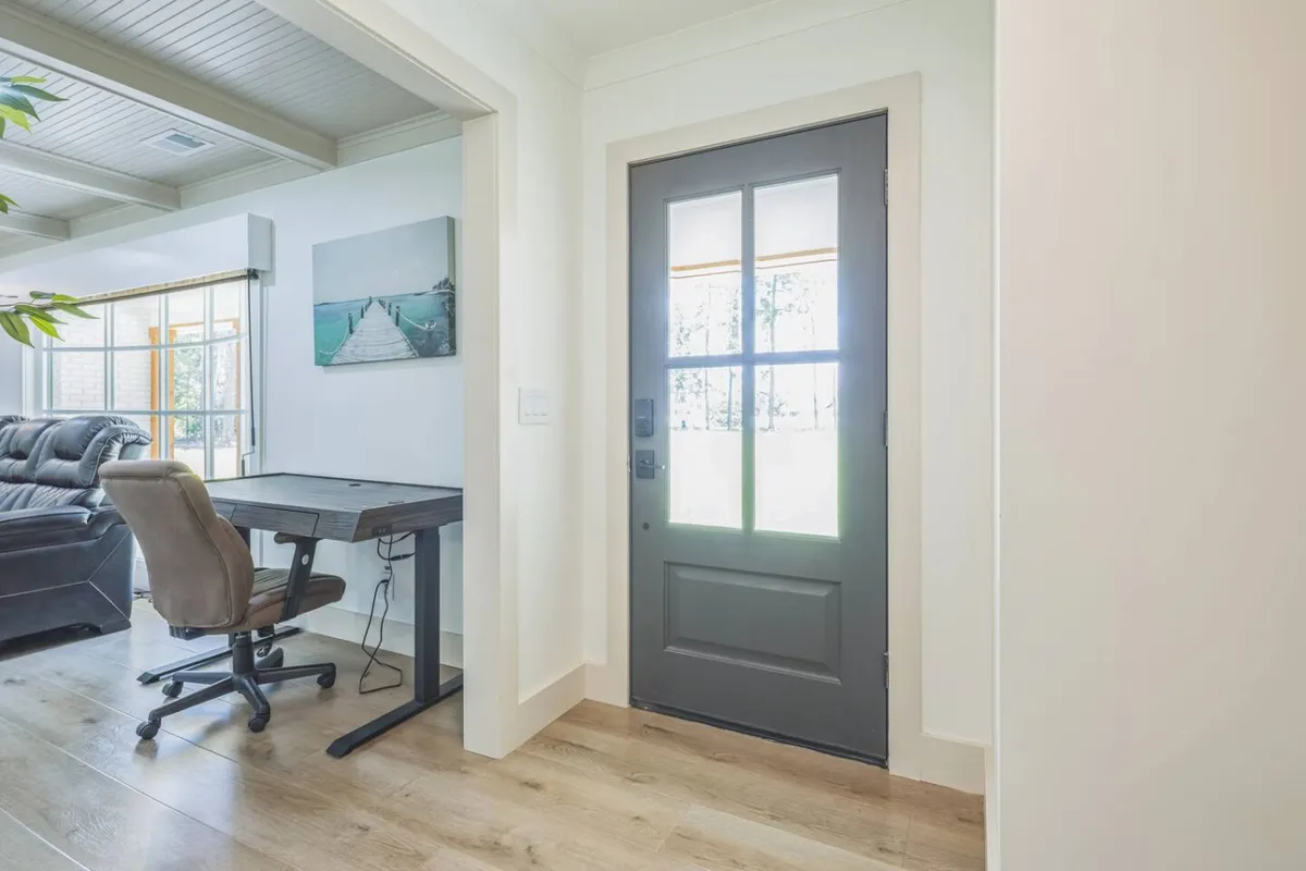 A bright, inviting entryway features a desk with a comfortable chair, artwork, and plenty of natural light. The setup hints at a productive workspace where remote workers can focus while enjoying the ambiance of the home.