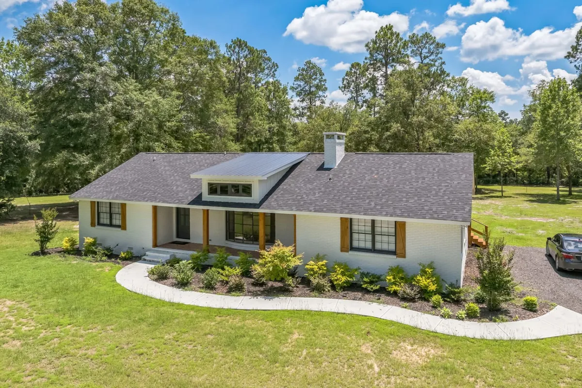 The image shows the welcoming facade of a modern single-family house, with a spacious front porch overlooking a beautifully landscaped garden. The setting is peaceful and secluded, with sunset light casting a warm glow over the lawn, inviting guests to relax outdoors and enjoy nature.