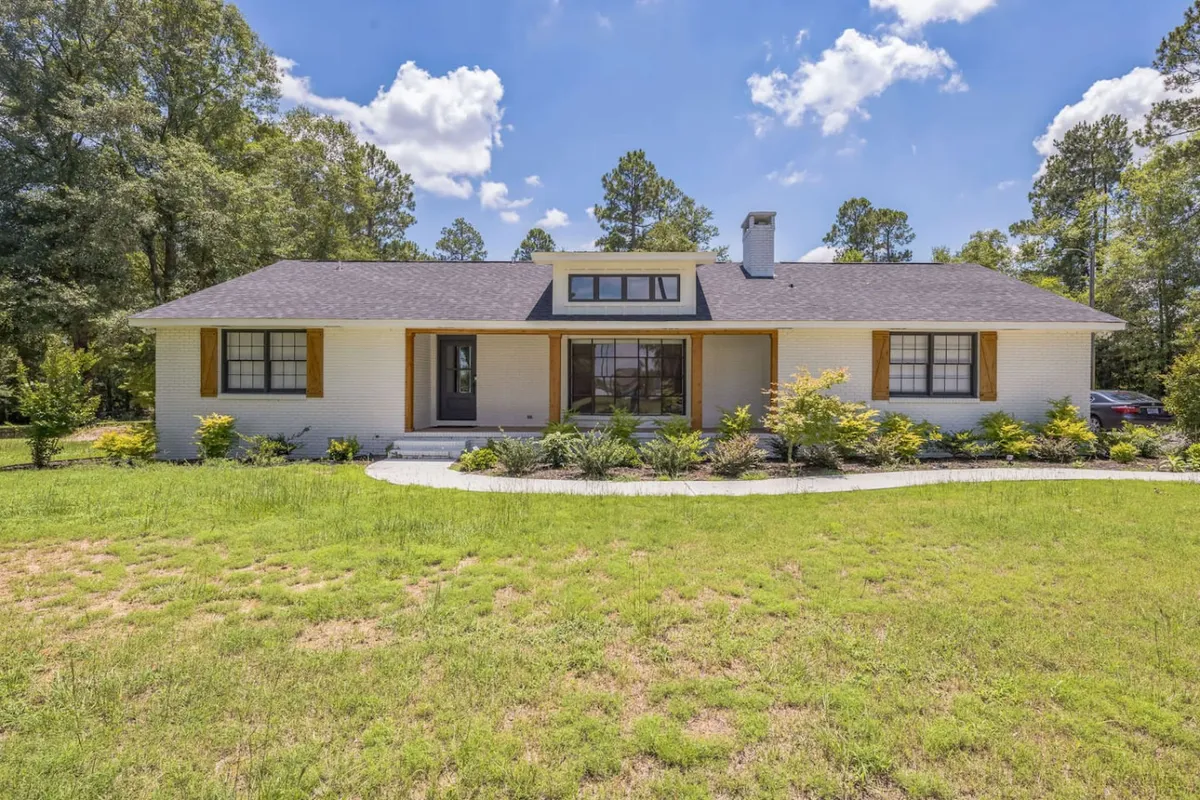 The image features a welcoming front porch with large windows and a landscaped garden, emphasizing outdoor relaxation and a sense of arrival. The porch and garden setting evoke feelings of comfort and homeliness, while the inviting façade connects the home to its serene environment.