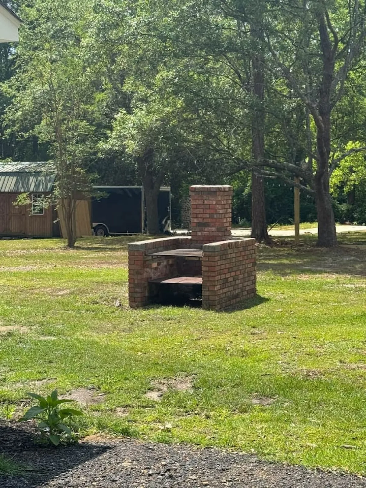 This image presents a brick grill area surrounded by greenery and a wooden structure in the background, suggesting opportunities for barbecuing, gathering with loved ones, and enjoying evenings under the stars. The atmosphere is relaxed and ideal for outdoor family time.