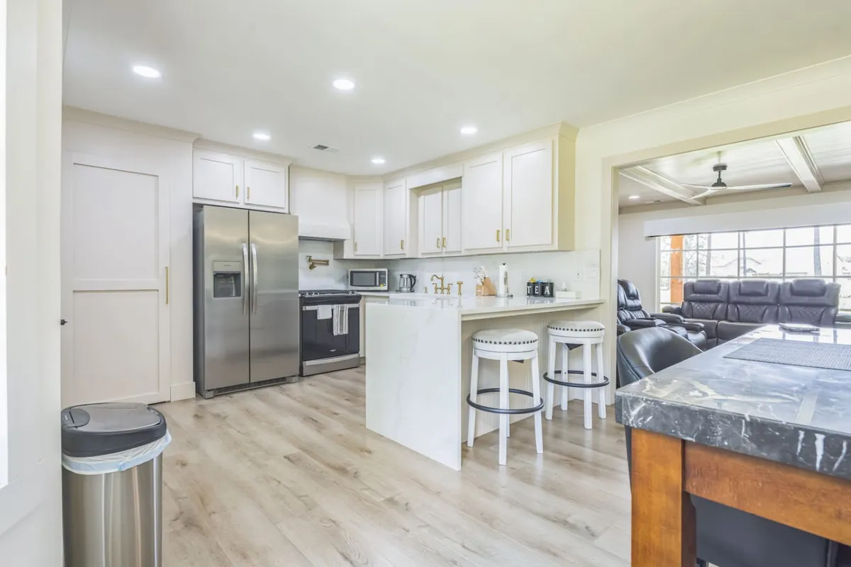 A spacious kitchen with a central island, stainless steel appliances, and bar stools, flooded with natural light from large windows. The setup invites both cooking and casual socializing, highlighting the heart of the home.
