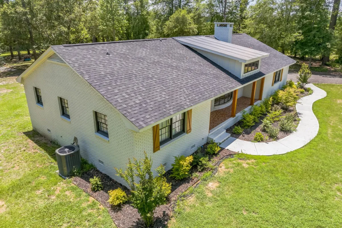 A welcoming view of the home's brick facade, distinctive roofline, and a landscaped pathway leading to the entrance. The cozy front porch is surrounded by lush greenery, with ample space for sipping morning coffee or relaxing in the evening.
