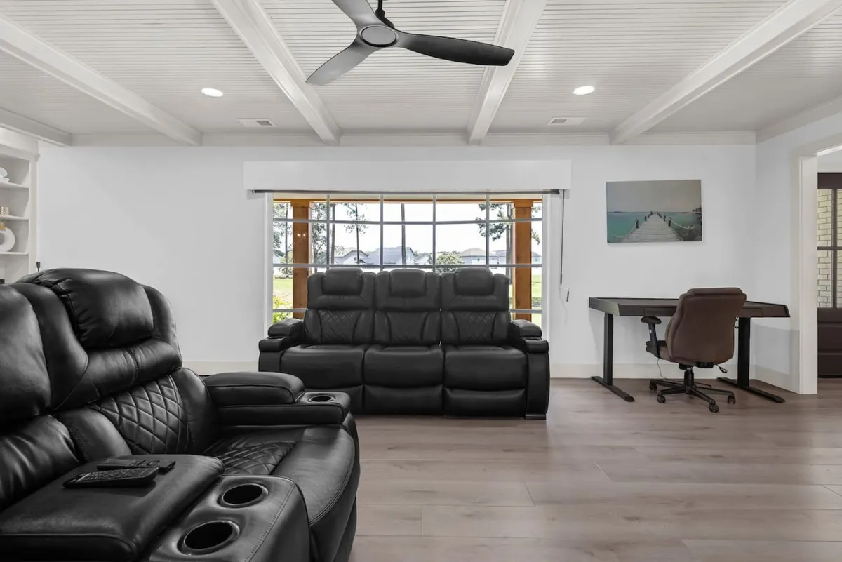 A cozy, inviting room featuring black leather recliners set near a large window that lets in ample natural light. A minimalist desk is positioned for remote work or casual conversations, while the view outside offers serene nature vistas, creating a comfortable, multipurpose environment.