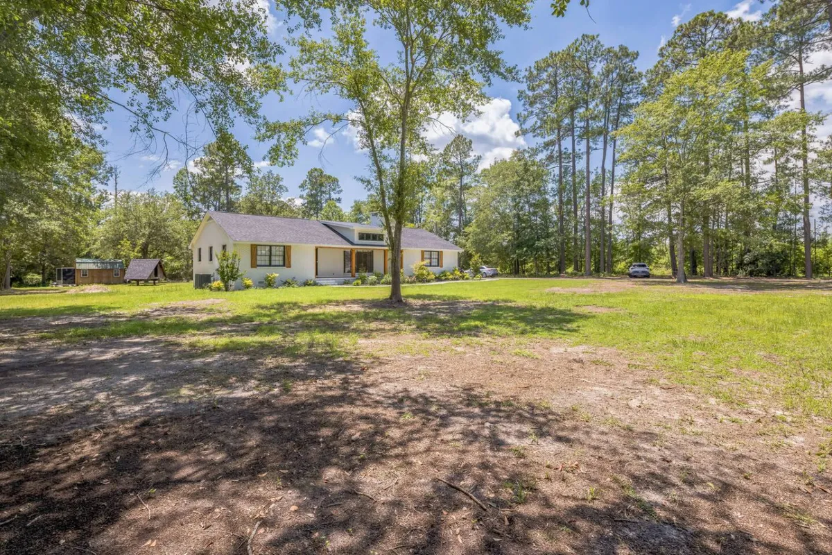 A wide view of the house nestled in lush South Carolina countryside, surrounded by a canopy of mature trees and an open, expansive yard. The setting exudes tranquility and provides ample space for outdoor games, family activities, and nature observation.