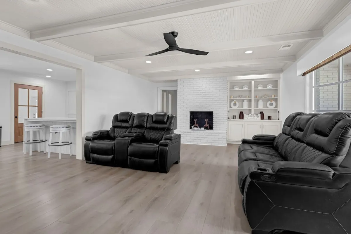 A modern, cozy living area features black recliners, a white brick fireplace, and built-in shelving. The space exudes comfort, making it an ideal spot for relaxing with entertainment or unwinding after a day of work.